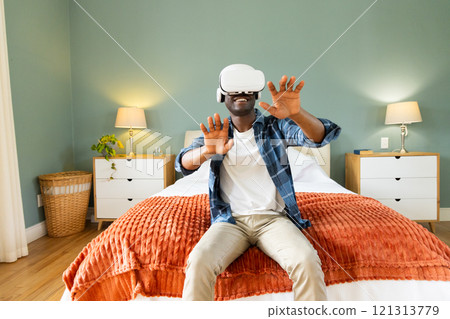 African American man enjoying virtual reality headset experience at home on bed African American man enjoying virtual reality headset experience at home on bed 121313779