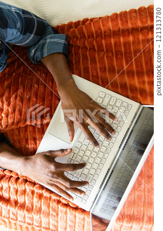 Typing on laptop, African american man working from home on cozy orange blanket 121313780