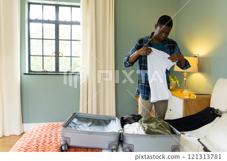 African American man packing suitcase in bedroom, preparing for holiday travel, at home African American man packing suitcase in bedroom, preparing for holiday travel, at home 121313781