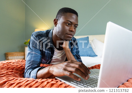 African American man using laptop on bed, focusing on work at home African American man using laptop on bed, focusing on work at home 121313782