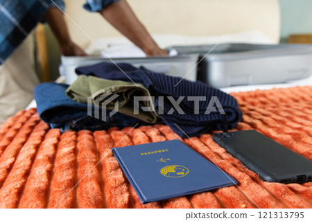 African american man, packing on bed with passport and phone, preparing for holiday travel, at home 121313795