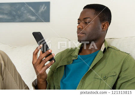 Relaxing at home, African american man using smartphone while sitting on comfortable couch 121313815