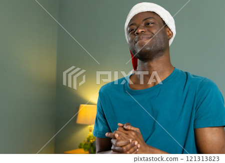 Christmas time, Smiling African american man wearing Santa hat enjoying festive moment at home Christmas time, Smiling African american man wearing Santa hat enjoying festive moment at home 121313823
