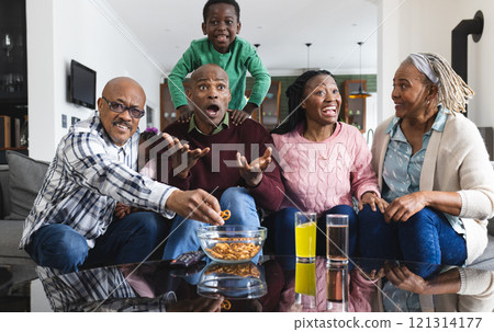 Excited african american parents, son and grandparents watching sport on tv, slow motion 121314177