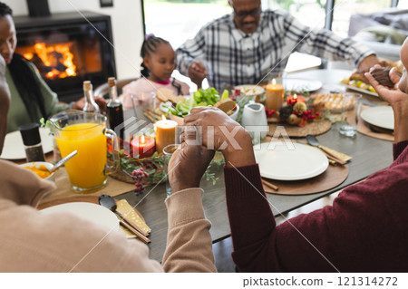 Happy african american multi generation family holding hands at thanksgiving dinner 121314272