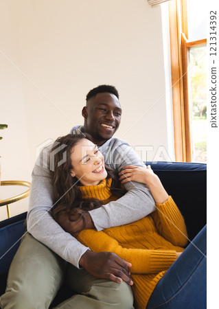 Happy diverse couple sitting on sofa embracing and smiling at home 121314392