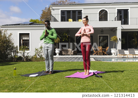 Diverse couple practicing yoga and meditating in garden 121314413