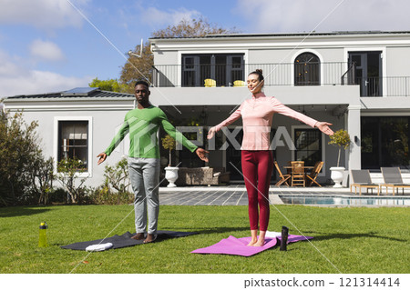 Diverse couple practicing yoga and stretching in garden 121314414