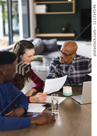 Diverse couple and biracial male financial advisor using laptop and discussing documents at home 121314546