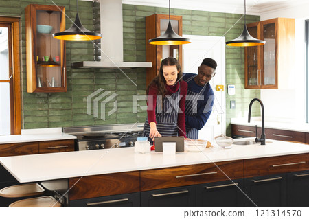 Happy diverse couple baking together in kitchen, using tablet at home, copy space Happy diverse couple baking together in kitchen, using tablet at home, copy space 121314570