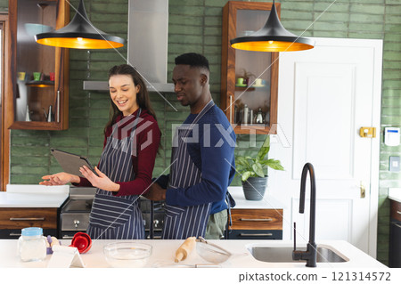 Happy diverse couple baking together in kitchen, using tablet at home, copy space 121314572