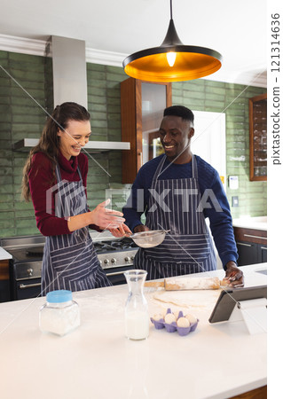 Happy diverse couple baking together in kitchen, using tablet at home 121314636