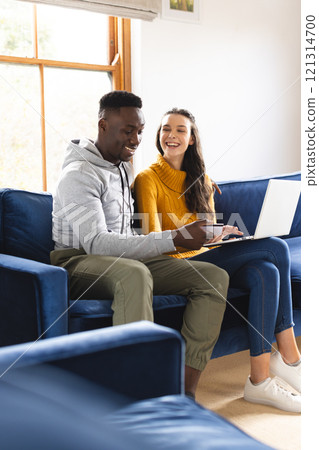 Happy diverse couple sitting on sofa using laptop for online shopping at home 121314700