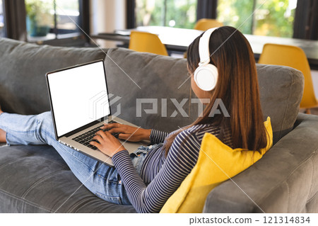 Biracial teenage girl wearing headphones and using laptop with copy space Biracial teenage girl wearing headphones and using laptop with copy space 121314834