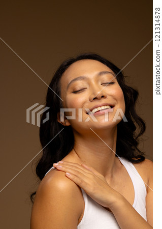 Happy asian woman with dark hair, with hand on shoulder and eyes closed, copy space 121314878