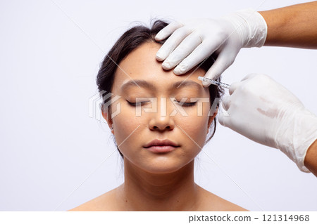 Hands of beautician in white surgical gloves injecting botox in brow of asian woman, copy space Hands of beautician in white surgical gloves injecting botox in brow of asian woman, copy space 121314968