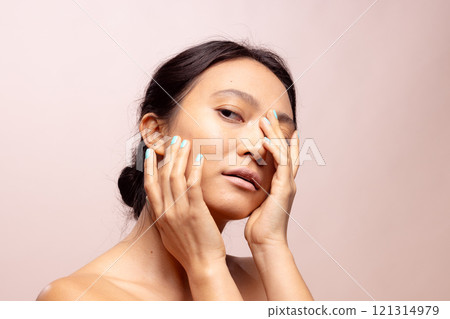 Asian woman with dark hair wearing blue nail varnish touching face with hands 121314979