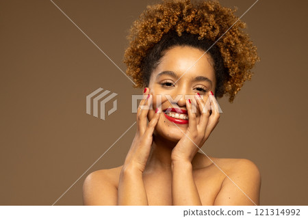 Happy biracial woman wearing red lipstick and nail varnish touching face with hands, copy space 121314992