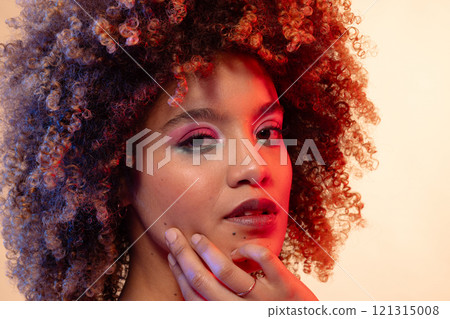 Biracial woman with curly hair wearing pink eyeshadow and lipstick touching face Biracial woman with curly hair wearing pink eyeshadow and lipstick touching face 121315008