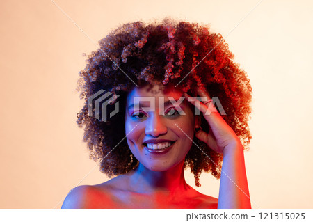 Biracial woman with curly hair, makeup touches head in red and blue light Biracial woman with curly hair, makeup touches head in red and blue light 121315025