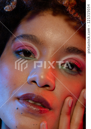 Close up of biracial woman with curly hair wearing eyeshadow and lipstick touching face 121315034