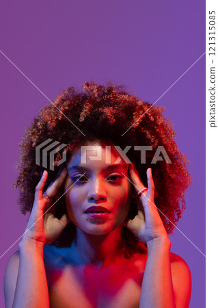 Biracial woman with curly hair, touching temples, in red and blue light with purple copy space Biracial woman with curly hair, touching temples, in red and blue light with purple copy space 121315085