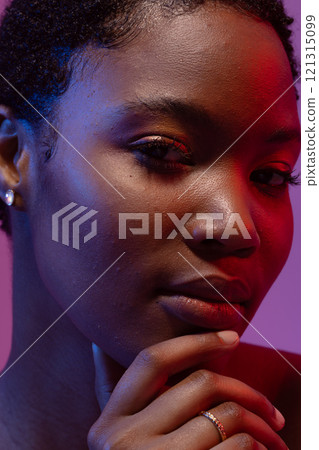 Close up of african american woman holding chin in red and blue light Close up of african american woman holding chin in red and blue light 121315099