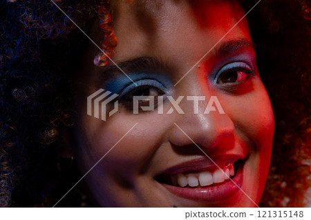 Close up of smiling biracial woman wearing blue eye shadow in red light Close up of smiling biracial woman wearing blue eye shadow in red light 121315148