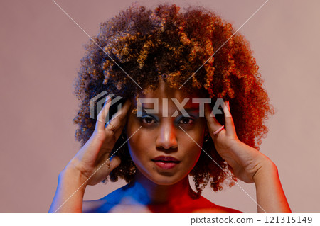 Biracial woman with curly hair touching temples in blue and red light Biracial woman with curly hair touching temples in blue and red light 121315149