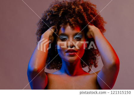 Biracial woman in blue eye shadow with hands in curly hair in blue and red light Biracial woman in blue eye shadow with hands in curly hair in blue and red light 121315150