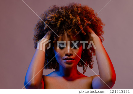 Biracial woman in blue eye shadow with eyes closed and hands in curly hair in blue and red light Biracial woman in blue eye shadow with eyes closed and hands in curly hair in blue and red light 121315151