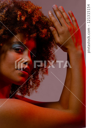 Biracial woman holding curly hair in red light Biracial woman holding curly hair in red light 121315154