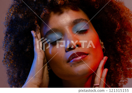 Biracial woman in blue eye shadow touching face with eyes closed in blue and red light Biracial woman in blue eye shadow touching face with eyes closed in blue and red light 121315155
