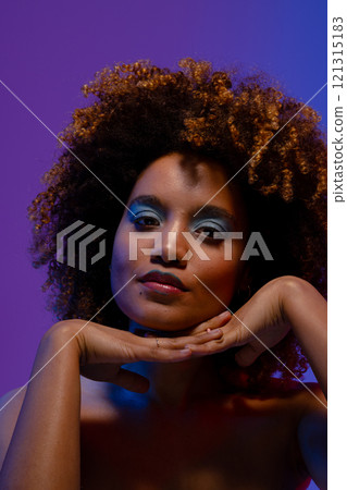 Biracial woman with curly hair and blue eye shadow with hands under chin 121315183