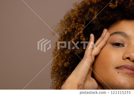 Half portrait of biracial woman with curly hair touching face, copy space 121315255