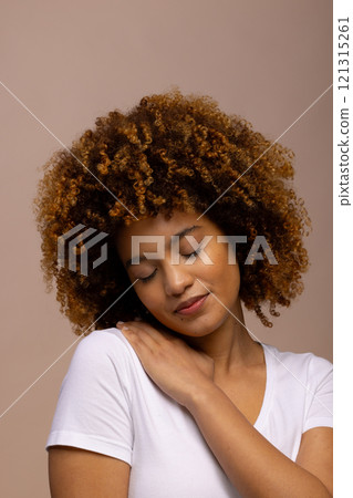 Smiling biracial woman with curly hair with hand on shoulder and closed eyes 121315261