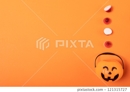 Close up of halloween candies over pumpkin shaped bucket against orange background Close up of halloween candies over pumpkin shaped bucket against orange background 121315727