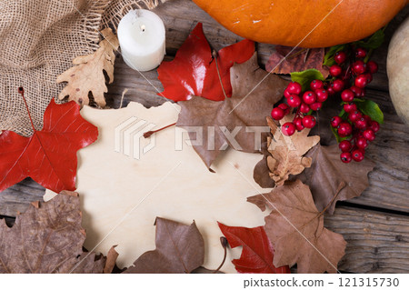 Paper with copy space, autumn leaves, pumpkin and berries on wooden surface against wooden surface 121315730