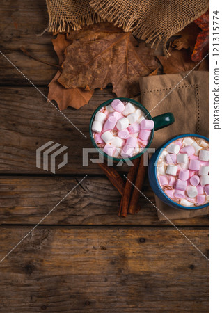 Hot chocolate drink filled with marshmallows in mugs by cinnamon, autumn leaves with copy space 121315774