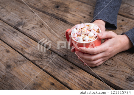 Cropped hands of woman holding mug of hot chocolate drink and marshmallows at table with copy space Cropped hands of woman holding mug of hot chocolate drink and marshmallows at table with copy space 121315784