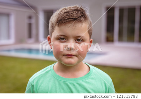Portrait of caucasian boy with blank expression standing at backyard outside house Portrait of caucasian boy with blank expression standing at backyard outside house 121315788