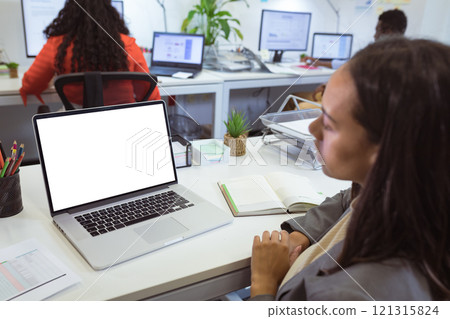 Biracial businesswoman sitting at desk using laptop with copy space in modern office 121315824