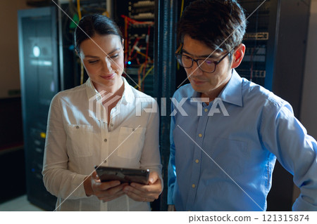 Diverse male and female engineers using digital tablet in computer server room 121315874
