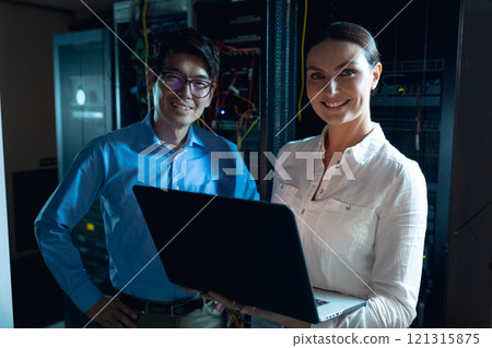 Portrait of diverse male and female engineers with laptop smiling in computer server room Portrait of diverse male and female engineers with laptop smiling in computer server room 121315875