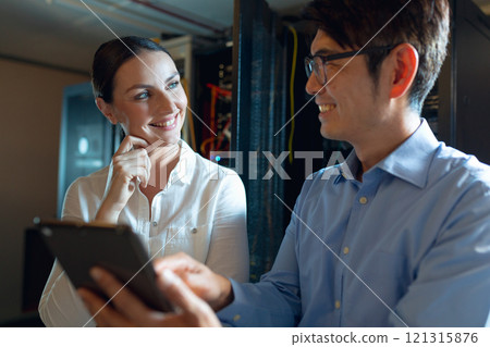 Diverse male and female engineers smiling while using digital tablet in computer server room 121315876