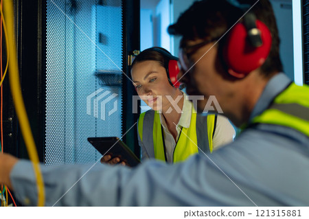 Diverse male and female engineer using digital tablet while inspecting in computer server room 121315881