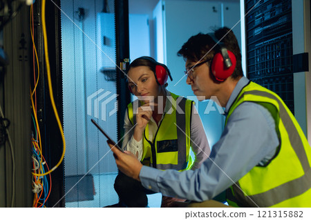 Diverse male and female engineer using digital tablet while inspecting in computer server room Diverse male and female engineer using digital tablet while inspecting in computer server room 121315882