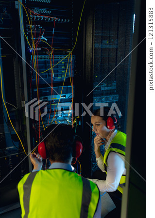 Diverse male and female engineers discussing together while inspecting iin computer server room Diverse male and female engineers discussing together while inspecting iin computer server room 121315883