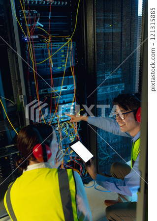 Diverse male and female engineer using digital tablet while inspecting in computer server room Diverse male and female engineer using digital tablet while inspecting in computer server room 121315885