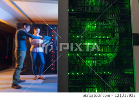 Diverse male and female engineers using laptop in computer server room 121315922